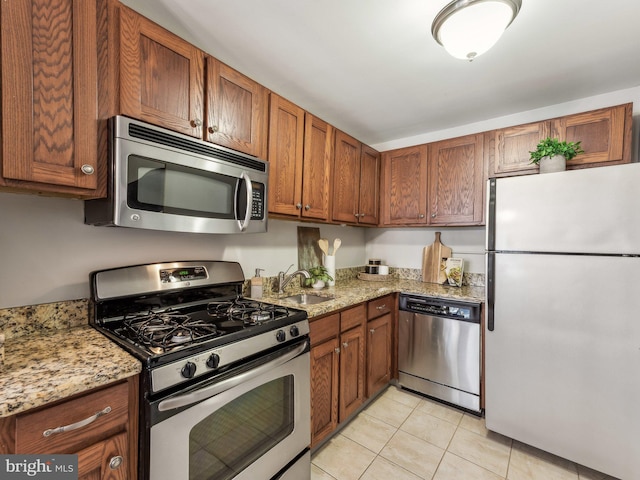 kitchen with sink, light tile patterned flooring, light stone counters, and stainless steel appliances