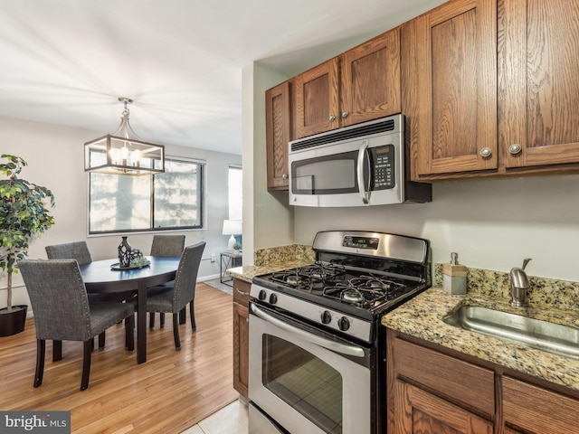 kitchen with light stone countertops, appliances with stainless steel finishes, sink, a chandelier, and light hardwood / wood-style flooring