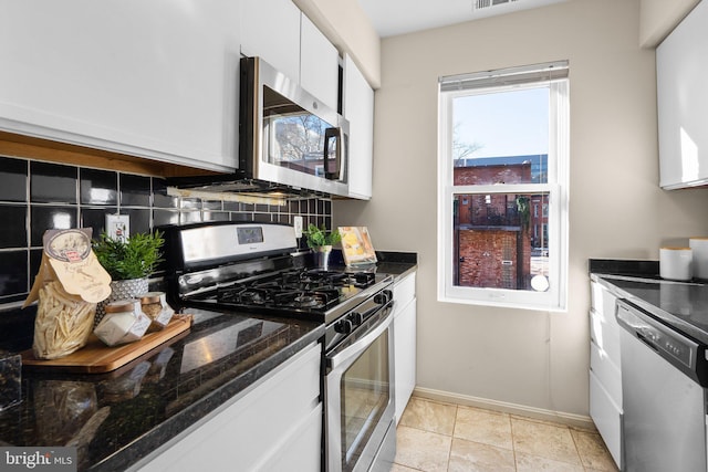 kitchen featuring white cabinetry, stainless steel appliances, dark stone counters, decorative backsplash, and light tile patterned flooring