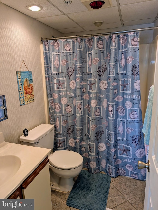 bathroom with tile patterned floors, a drop ceiling, toilet, and vanity