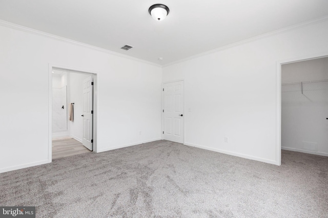 unfurnished bedroom with light carpet, ensuite bath, ornamental molding, a spacious closet, and a closet