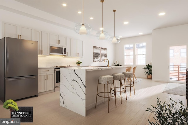 kitchen featuring stainless steel appliances, tasteful backsplash, an island with sink, decorative light fixtures, and white cabinets