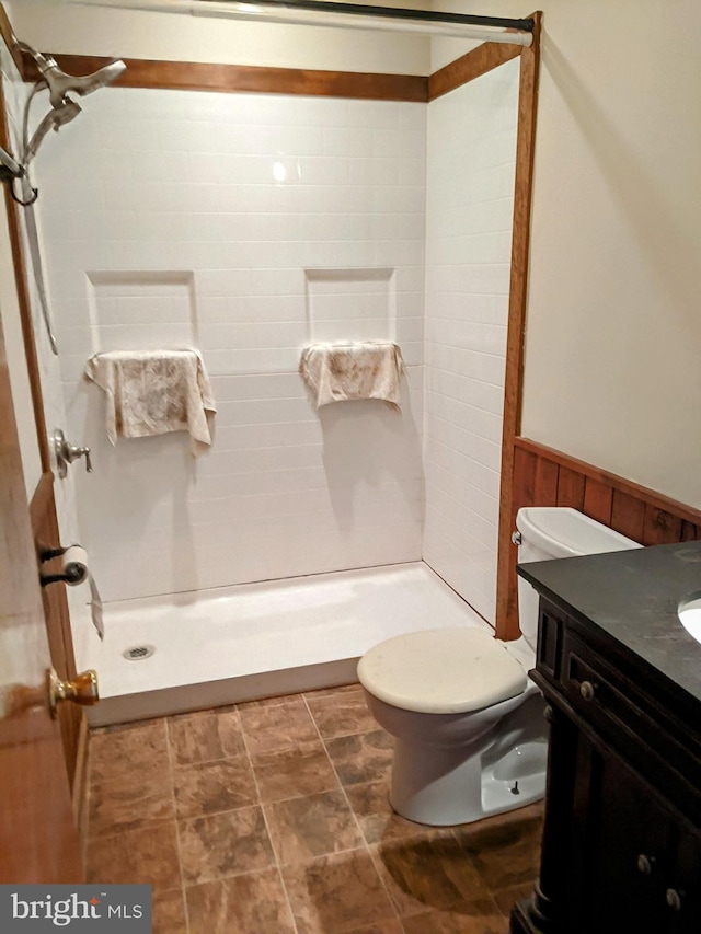 bathroom with wood walls, toilet, vanity, and a tile shower