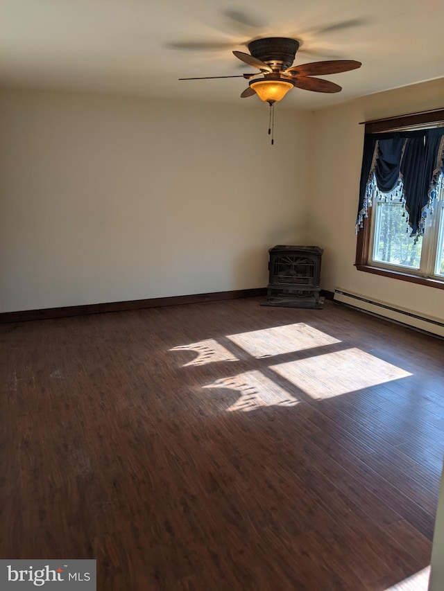 unfurnished room featuring ceiling fan, baseboard heating, dark hardwood / wood-style floors, and a wood stove