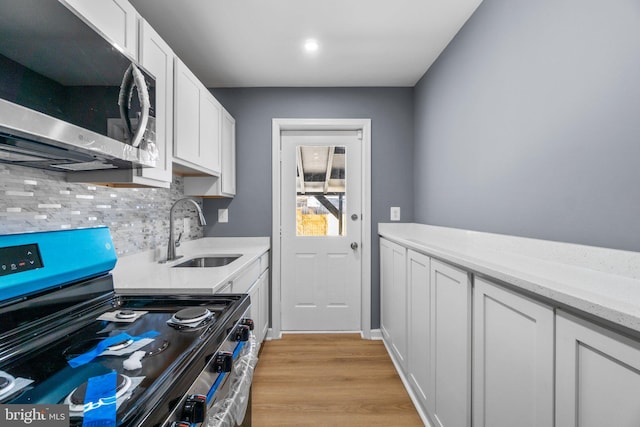 kitchen with stove, white cabinets, sink, tasteful backsplash, and light hardwood / wood-style floors