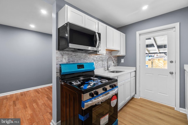 kitchen featuring gas stove, white cabinetry, sink, tasteful backsplash, and light hardwood / wood-style floors