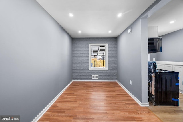 spare room with light hardwood / wood-style floors and brick wall