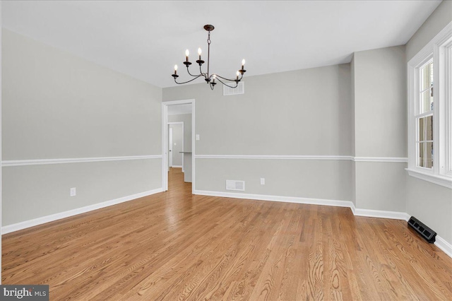 spare room featuring light hardwood / wood-style flooring and a chandelier