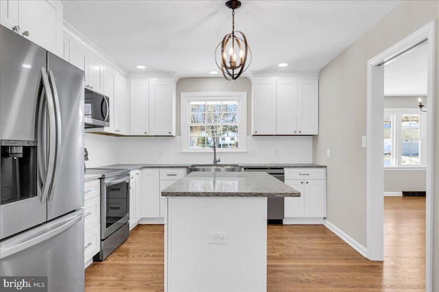 kitchen featuring light stone countertops, stainless steel appliances, white cabinetry, a kitchen island, and hanging light fixtures