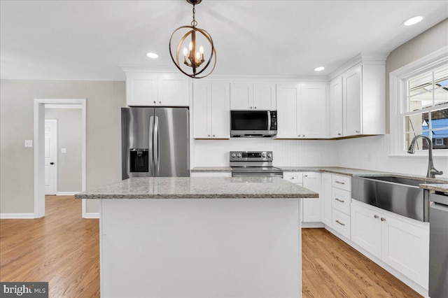 kitchen with light stone countertops, appliances with stainless steel finishes, a center island, white cabinetry, and hanging light fixtures