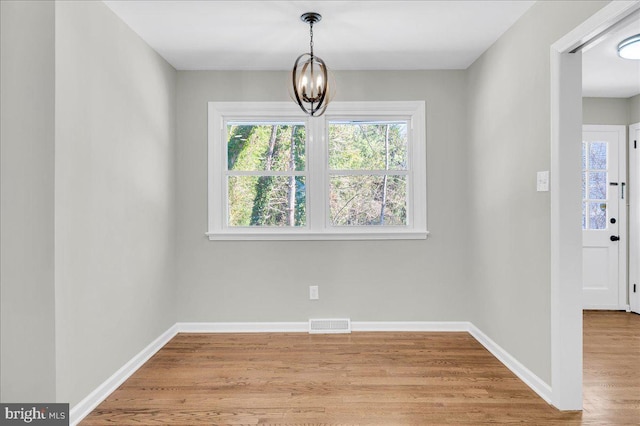 unfurnished dining area featuring wood-type flooring and an inviting chandelier