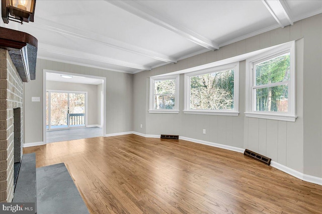 unfurnished living room featuring beam ceiling, a fireplace, wood-type flooring, and plenty of natural light