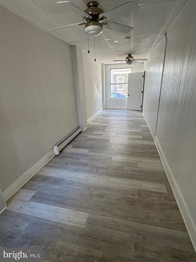 hall with wood walls, a baseboard heating unit, and wood finished floors