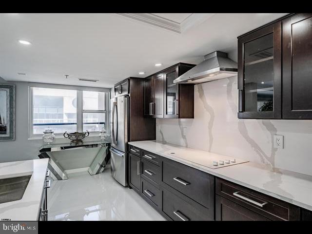 kitchen with stainless steel refrigerator, white cooktop, dark brown cabinets, and wall chimney range hood