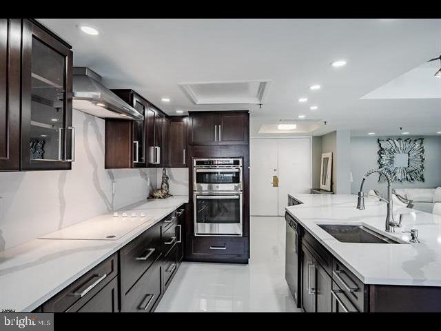 kitchen featuring appliances with stainless steel finishes, sink, dark brown cabinets, and wall chimney range hood