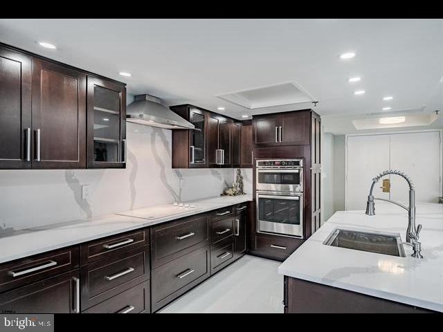 kitchen featuring wall chimney exhaust hood, sink, stovetop, double oven, and backsplash