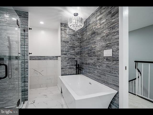 bathroom with tile walls, separate shower and tub, and an inviting chandelier