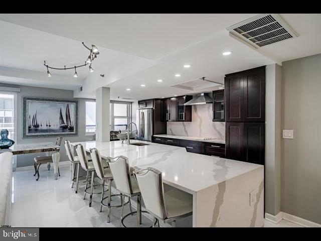 kitchen with wall chimney range hood, sink, stainless steel refrigerator, a spacious island, and a kitchen bar