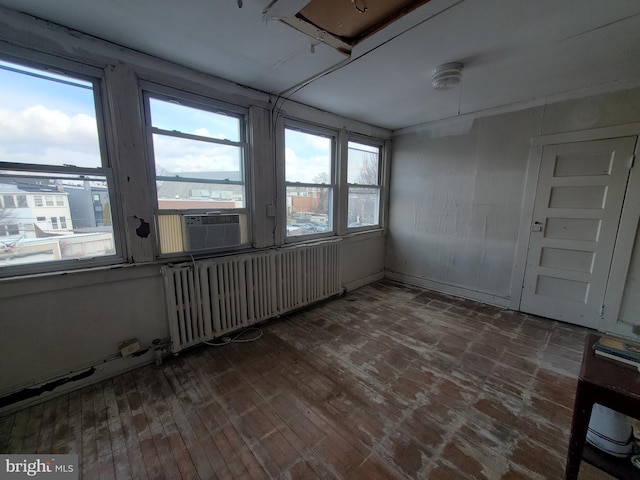 empty room featuring radiator, dark wood-type flooring, and a healthy amount of sunlight