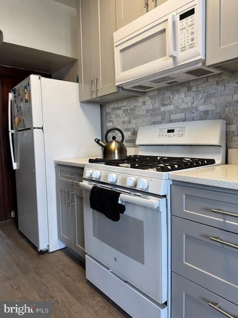 kitchen featuring gray cabinets, dark hardwood / wood-style flooring, backsplash, and white appliances