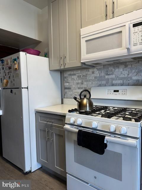 kitchen with gray cabinetry, decorative backsplash, dark hardwood / wood-style flooring, and white appliances