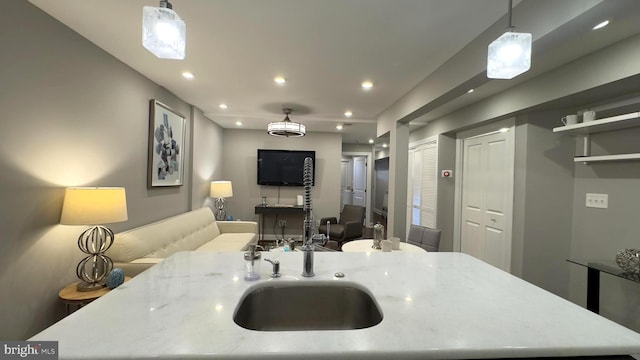 kitchen featuring a center island with sink, light stone counters, hanging light fixtures, and sink