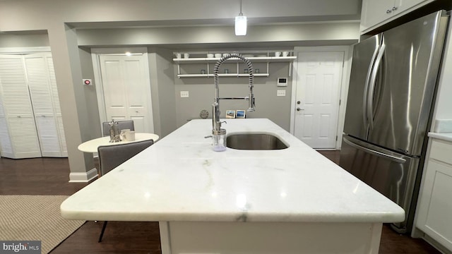 kitchen featuring stainless steel fridge, light stone counters, sink, decorative light fixtures, and a center island with sink