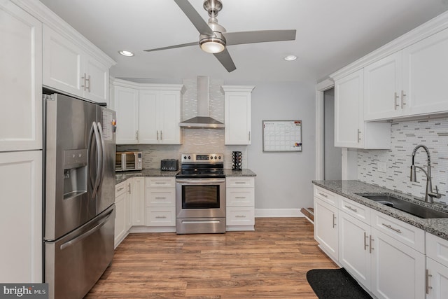 kitchen with white cabinetry, sink, wall chimney exhaust hood, stainless steel appliances, and dark stone countertops