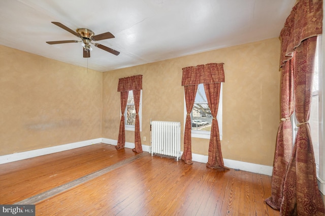 spare room featuring hardwood / wood-style floors, radiator, a ceiling fan, and baseboards