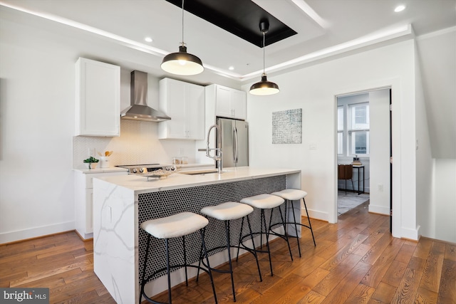 kitchen featuring a kitchen island with sink, white cabinets, wall chimney range hood, sink, and stainless steel refrigerator