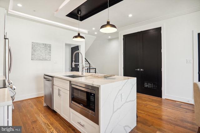 kitchen with light stone countertops, stainless steel appliances, sink, hanging light fixtures, and an island with sink