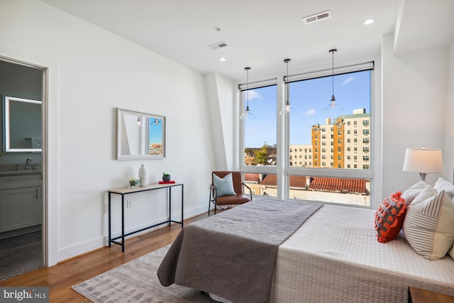 bedroom with connected bathroom, multiple windows, wood-type flooring, and a wall of windows