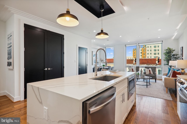 kitchen with light stone countertops, stainless steel appliances, sink, hanging light fixtures, and an island with sink