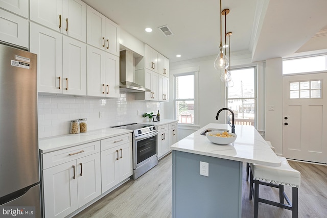 kitchen featuring backsplash, stainless steel appliances, wall chimney range hood, sink, and a center island with sink