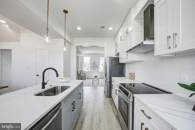 kitchen with sink, wall chimney range hood, decorative light fixtures, white cabinets, and appliances with stainless steel finishes