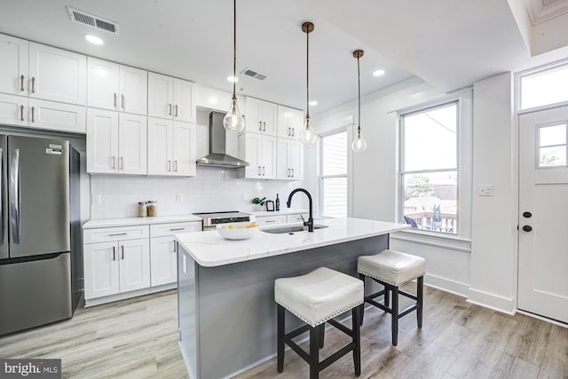 kitchen featuring sink, wall chimney exhaust hood, an island with sink, white cabinets, and appliances with stainless steel finishes