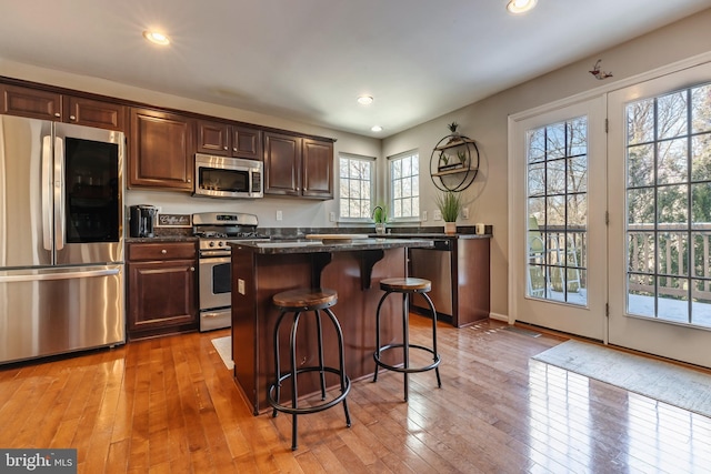 kitchen with a kitchen bar, appliances with stainless steel finishes, light hardwood / wood-style flooring, dark stone countertops, and a center island