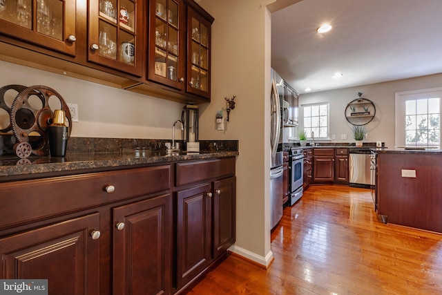 bar featuring dark stone countertops, appliances with stainless steel finishes, and light hardwood / wood-style flooring