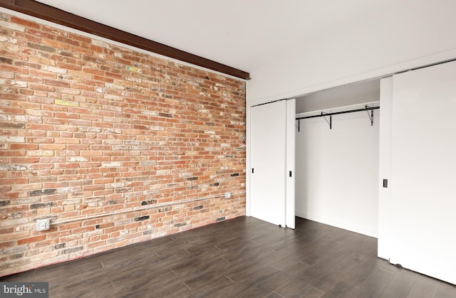 unfurnished bedroom with dark hardwood / wood-style floors, a closet, and brick wall