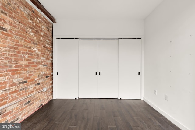 unfurnished bedroom featuring a closet, dark wood-type flooring, and brick wall