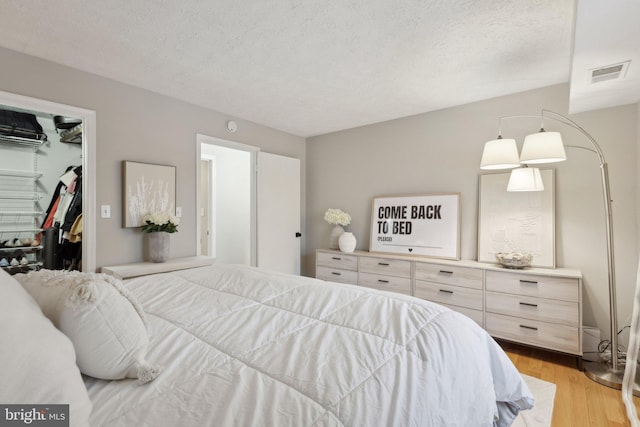 bedroom featuring light wood-type flooring, a walk in closet, a closet, and a textured ceiling