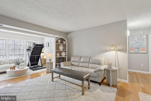 living room featuring light wood-type flooring, a textured ceiling, and built in shelves