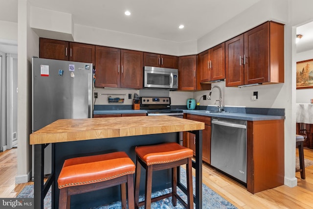 kitchen with wood counters, stainless steel appliances, light wood-type flooring, a breakfast bar, and sink