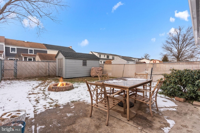 snow covered patio with an outdoor fire pit and a shed