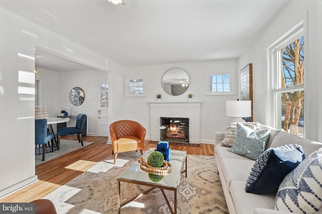 living room with a brick fireplace, ceiling fan, and light hardwood / wood-style flooring