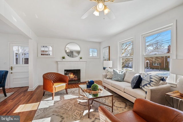 living room featuring ceiling fan, wood-type flooring, and a brick fireplace