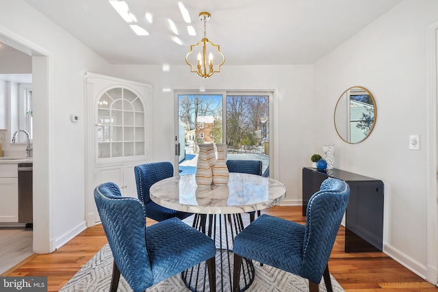 dining space featuring light wood-type flooring, sink, and an inviting chandelier