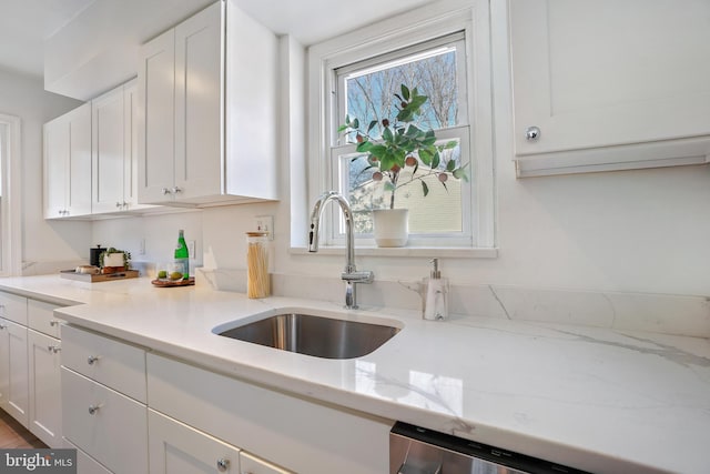 kitchen with stainless steel dishwasher, light stone countertops, white cabinetry, and sink