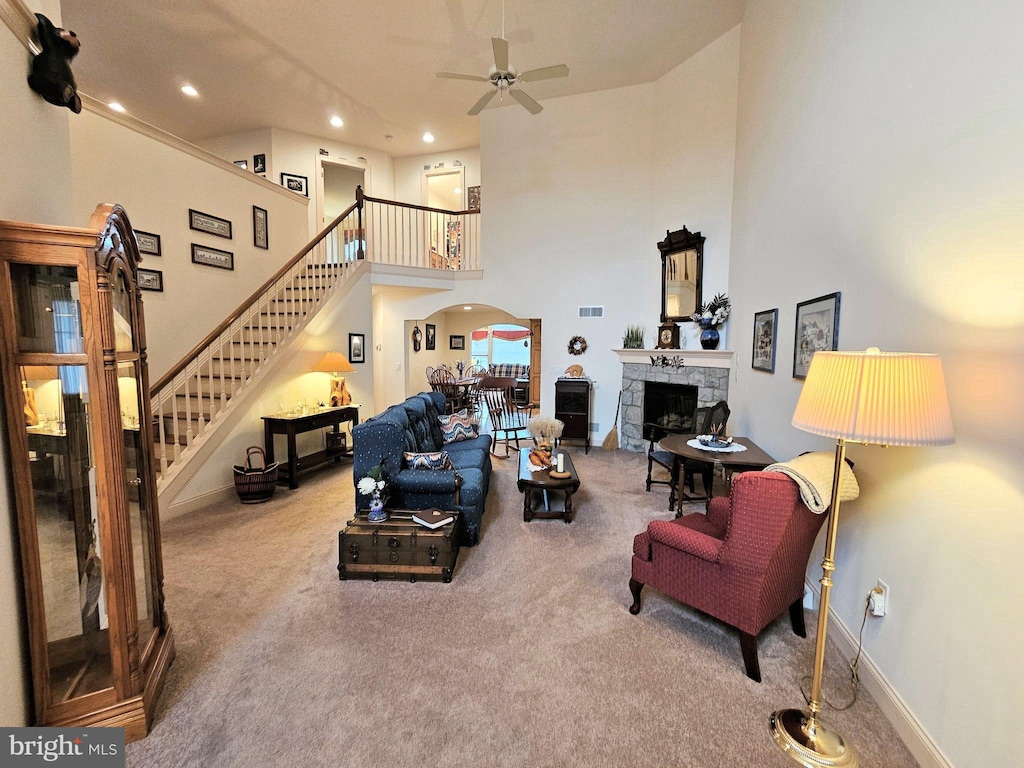 carpeted living room with ceiling fan, a high ceiling, and a stone fireplace