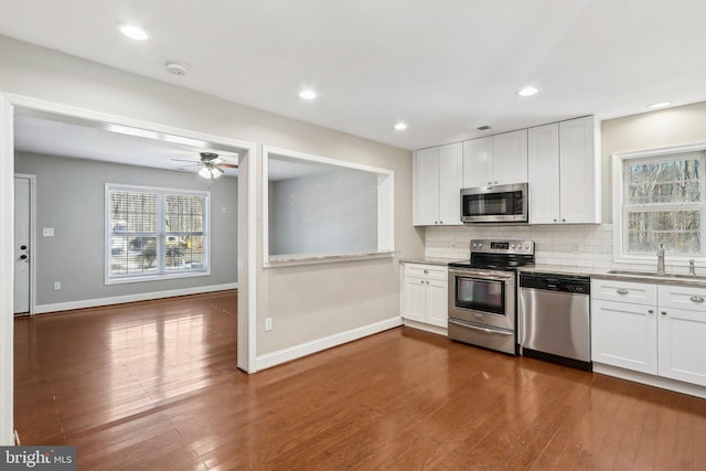 kitchen with appliances with stainless steel finishes, sink, white cabinets, dark hardwood / wood-style flooring, and backsplash